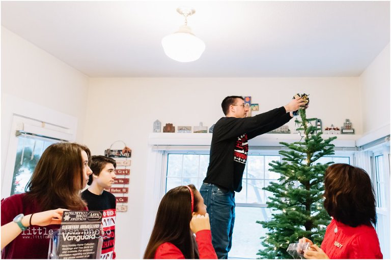 man places topper on Christmas tree while family watches on